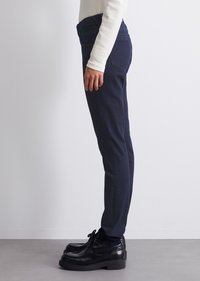 Tummansinisiä farkkuhousuja, joissa on slim fit -malli, takataskut ja sileä pinta, yhdistettyinä mustiin nauhakenkiin.