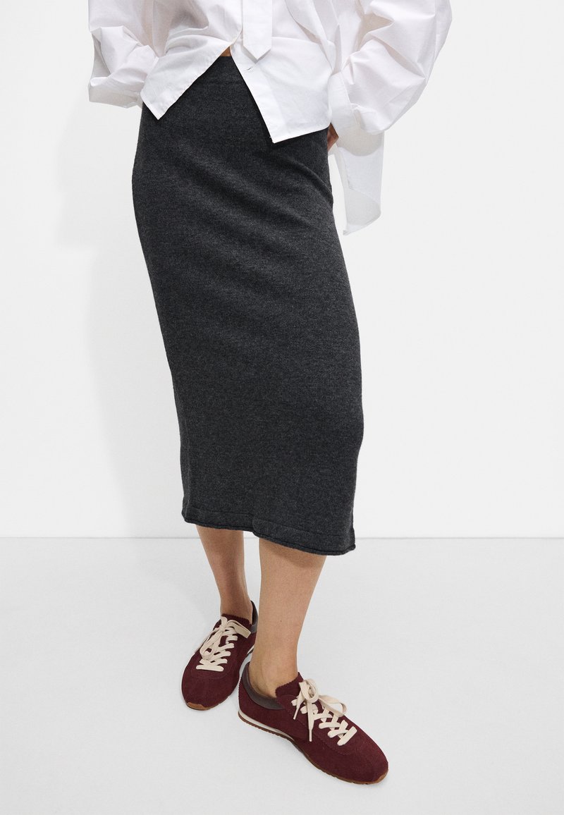 Szara spódnica midi z bawełnianej mieszanki o dopasowanym kroju, z prostym wykończeniem. W połączeniu z burgundowymi trampkami i białą, oversize'ową koszulą.