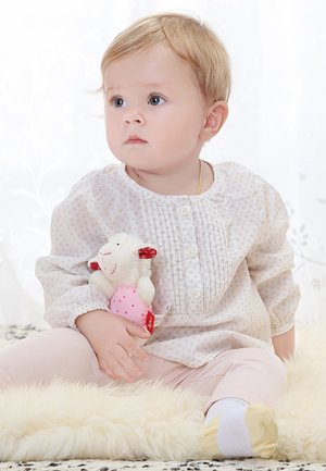 Light beige blouse with small patterns and pleats, paired with light pink pants. Holding a plush toy sheep with a pink dress.