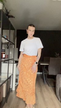 Saia laranja com bolinhas douradas, bainha franzida e cintura amarrada. Combinada com uma t-shirt branca. Tecido suave, design casual.