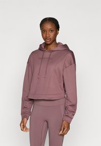 Afgekorte capuchontrui in mauve met het "Nike Pro" logo, voorzien van een capuchon met trekkoord en geribbelde boorden. Gecombineerd met bijpassende legging.