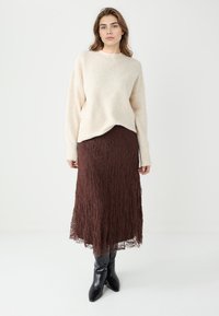 Pull beige clair texturé à manches longues, associé à une jupe brune en dentelle superposée et des bottes noires à bout pointu.