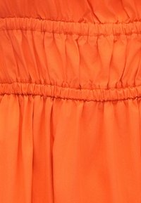 Oranžová tkanina na šaty s nariasenou textúrou a elastickým pásom. Hladký povrch s konzistentnou farbou, zdôrazňujúci záhyby a záhyby.