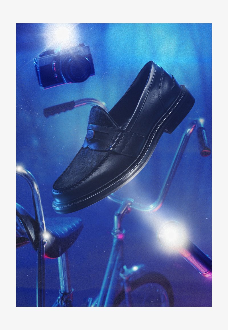 Sorte skinn loafers svevende over et vintage sykkelstyre og sete med et kamera som blinker i blått lys i bakgrunnen.