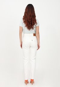Jeans blancos de pierna recta con una cintura alta, que presentan un parche de cuero en la parte trasera y una camiseta azul clara, combinados con sandalias de tacón bloque naranja.