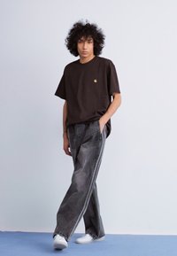 Zwarte katoenen T-shirt met een klein gouden logo, gecombineerd met grijze wijde jeans met witte zijkanten, gedragen met witte sneakers.