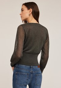 Pulover ajustat de culoare gri închis, cu mâneci din plasă texturată, tiv ondulat și decolteu rotund. Purtați-l cu blugi clasici albaștri.