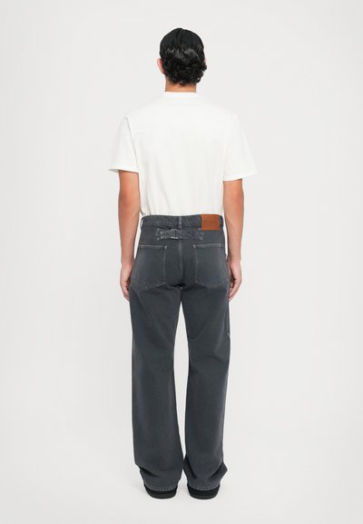 Witte t-shirt en donkergrijze wijde broek met een gebogen tailleband, twee achterzakken en een leren patch detail op de tailleband.