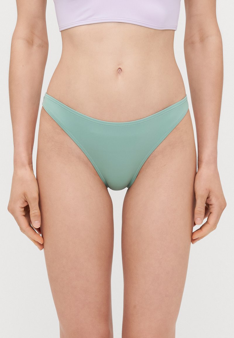 Mentazöld bikini alsó, sima, ruganyos anyagból készült. Alacsony derekú szabással és minimalista dizájnnal rendelkezik, amelyet kontrasztos derékrész emel ki.