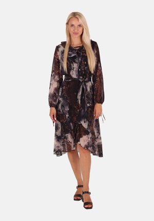 Transparenter, dunkler Blumenrock mit langen Ärmeln, einem Band am Hals und einem fließenden Saum. Getragen mit schwarzen, schnürbaren High Heels.