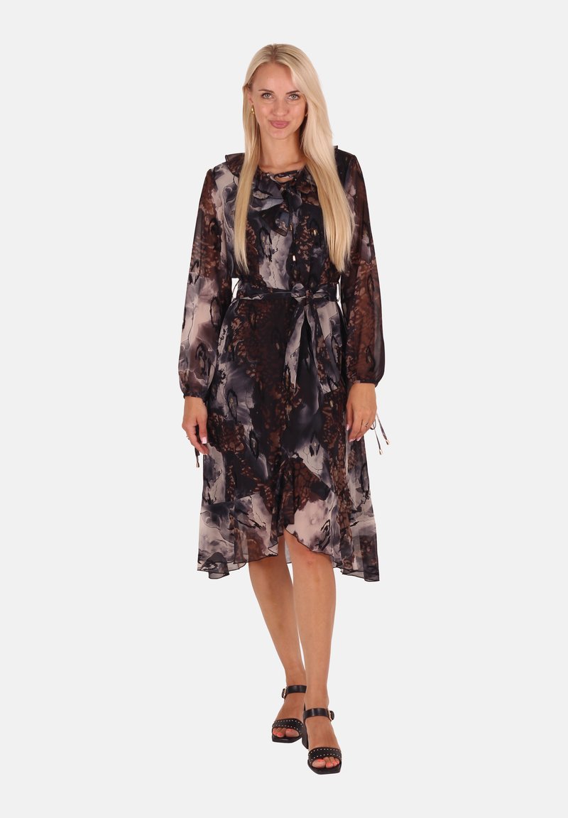 Transparenter, dunkler Blumenrock mit langen Ärmeln, einem Band am Hals und einem fließenden Saum. Getragen mit schwarzen, schnürbaren High Heels.