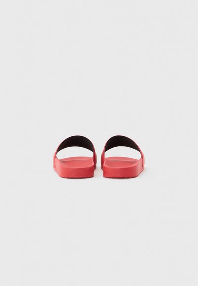 Paire de sandales mules rouges à dos ouvert avec semelles épaisses sur un fond gris neutre, vues de dos.