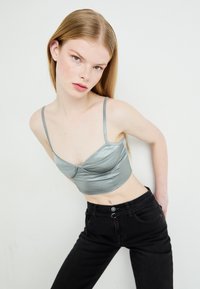 Siv svilen crop top z tankimi naramnicami, ki ima strukturiran bust in oprijet silhueto, v kombinaciji s črnimi hlačami z visokim pasom.