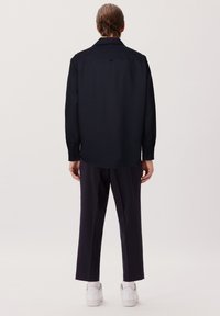 Navy-blaues Button-up-Hemd aus glattem Stoff, mit klassischem Kragen und langen Ärmeln. Kombiniert mit dunklen Hosen und weißen Sneakers.