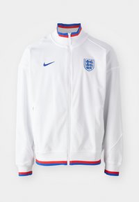 Biela bunda Nike s plným zipsom, modré akcenty na logu a golieri a červeno-modré pruhované lemovanie na manžetách a spodnom okraji.