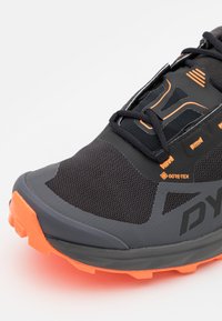 Scarpa da trail running nera con marchio Gore-Tex, dotata di suola arancione, pannelli in rete e superficie testurizzata con intersuola ammortizzata.