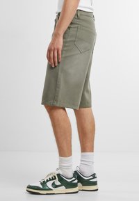 Shorts in denim verde a taglio dritto, con design a cinque tasche e orlo che cade appena sopra il ginocchio, abbinati a sneakers verdi e bianche.