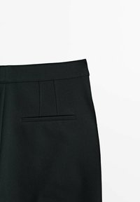 Pantalon noir sur mesure avec une texture lisse, doté d'un devant plat, de deux plis et d'une poche arrière discrète.