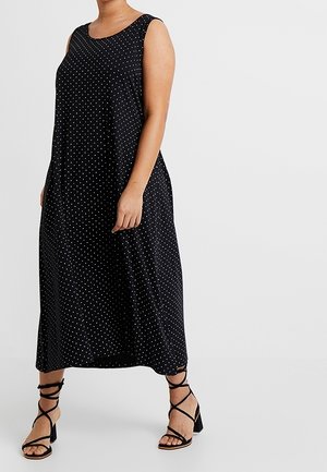 Sleeveless black maxi dress with white polka dots, worn with black strappy high-heeled sandals on plain light background.