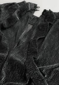 Material textil negru, cu textură și sclipici metalic, având margini ondulate și două butoane negre. Design moale și fluid cu un model ondulat.