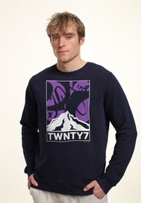 Tmavě modrá mikina s bílou grafikou hory a fialovými akcenty. Má kulatý výstřih a žebrované manžety a lem. Jednoduchý design.
