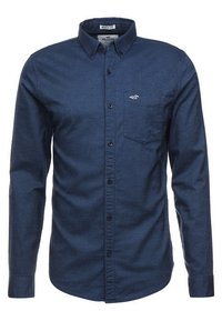 Triko s dlouhým rukávem ve svalovém střihu z tmavě modré látky, se zapínáním na knoflíky, límcem a kapsou na levé straně hrudi s detailem loga.