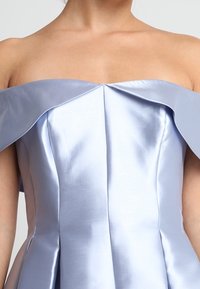 Žena v bezramínkových, světle modrých saténových šatech s překládaným výstřihem a strukturovaným korzetem.