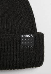 Căciulă tricotată neagră cu textură în relief. Are un etichetă rectangulară cu text alb "ERROR" și un model de puncte albe pe un fundal negru.