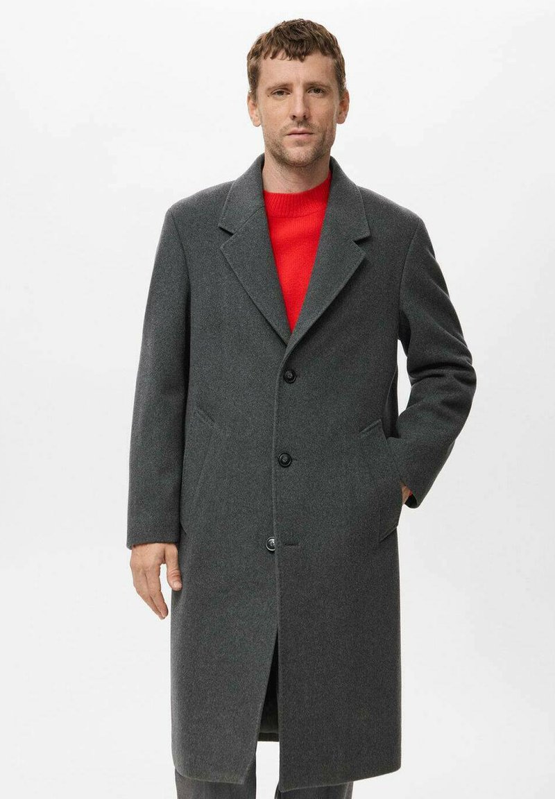 Cappotto grigio in lana con colletti a vista, bottoni frontali e tasche laterali, abbinato a un maglione rosso sotto.