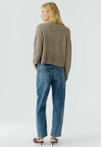 Bruine cropped trui met geribbelde zoom, gecombineerd met lichtblauwe recht gesneden jeans met twee achterzakken. Schoeisel: zwarte sandaaltjes met hak.