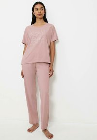 Różowa bawełniana koszulka z kwiatowym haftem, w połączeniu z dopasowanymi różowymi spodniami. Luźny krój, krótkie rękawy i miękka tekstura. Na bosaka.