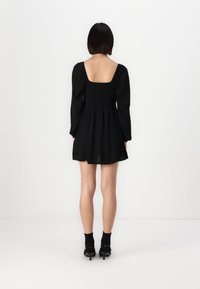 Melnā kleita ar kvadrātu izgriezumu, garām puff piedurknēm un smocked korseti. Svārki ir plūstoši, beidzoties virs ceļgaliem.