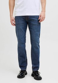 Jeans de mezclilla azul oscuro con un ajuste slim, con costuras sutiles y un diseño clásico de cinco bolsillos, combinados con zapatos negros de cordones.