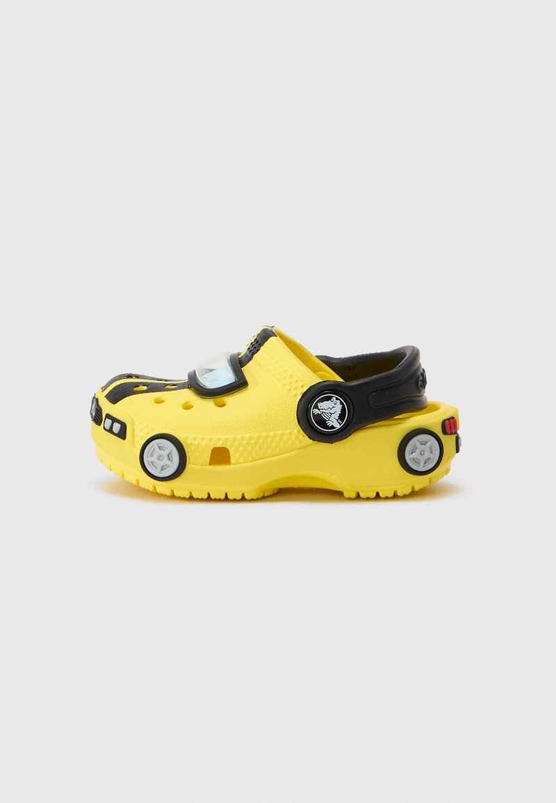 Sabot enfant jaune et noir stylisé comme un taxi avec des détails de roue et de phare et une bride de talon noire réglable.