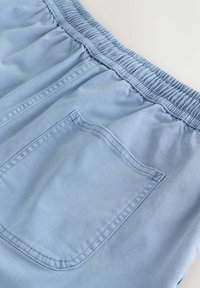 Pantalon bleu clair avec taille élastique et une seule poche arrière, présenté en gros plan sur un fond neutre.