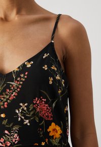 Svart blomstermønstret cami-top med tynne stropper, livlige flerfargede blomsterdesign og en jevn tekstur. Designet har V-hals.