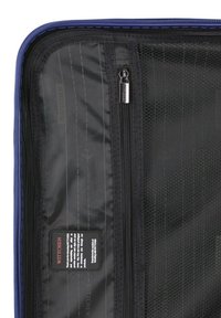 Black zipper compartments inside a blue suitcase, featuring a smooth texture, patterned mesh, and a care label stitched on the side.