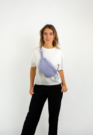 Sac banane lilas avec une texture lisse, une forme incurvée et une fermeture éclair. Dispose d'une bandoulière ajustable pour un port polyvalent.