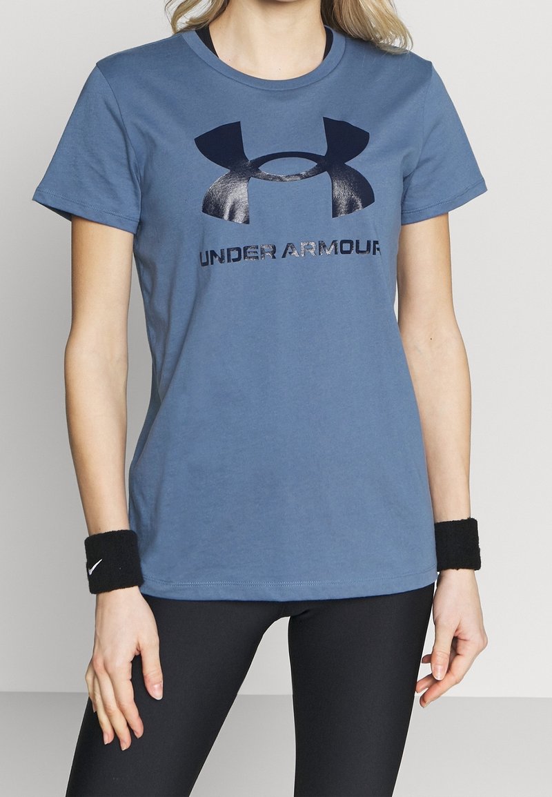 Modré bavlněné tričko s černým logem Under Armour a nápisem. Krátké rukávy a kulatý výstřih. Nosí se s černými legínami a náramky.
