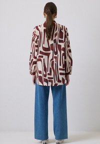 Langærmet skjorte i creme med abstrakt burgundy mønster, parret med brede blå denimjeans. Afslappet pasform med knaplukning ved håndleddene.
