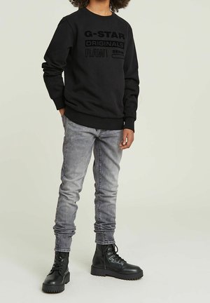 Black sweatshirt with embossed text logos, paired with light gray skinny jeans and black combat boots. Smooth fabric, casual fit.