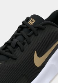 Sort sportsko med en tekstureret overdel, der har tonale snørebånd og et fremtrædende guld Nike swoosh på siden, hvid sål.