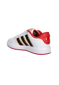 Białe sneakersy Adidas z czerwonym wykończeniem, czarnymi i żółtymi paskami oraz czerwoną twarzą Myszki Miki na zakładce obcasu, pokazane z bocznego tyłu.