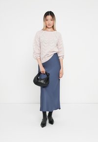 Jasnoróżowy sweter z dzianiny o teksturowanym wzorze liści, zestawiony z niebieską satynową spódnicą midi. Czarna torebka i szpilki dopełniają stylizację.