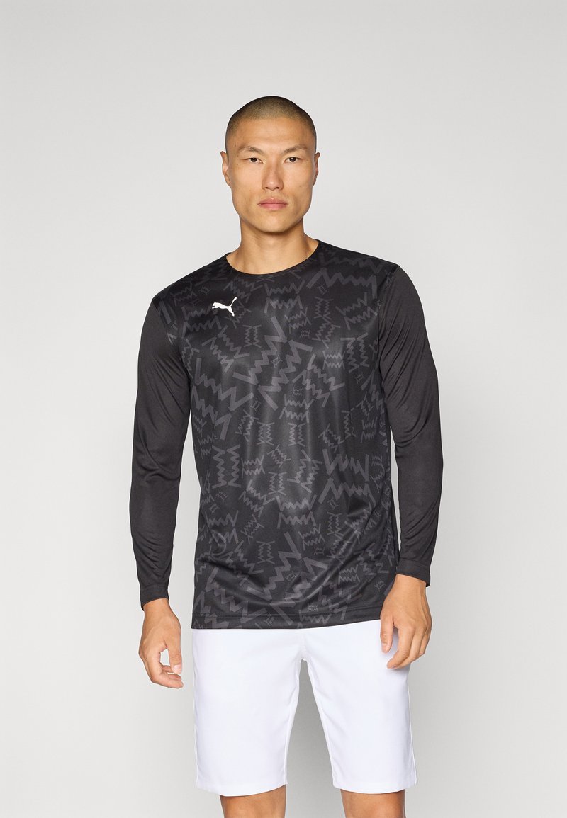 Zwarte sportshirt met lange mouwen en geometrische patronen, gemaakt van lichtgewicht materiaal. Witte logo op de linkerkant van de borst, gecombineerd met witte shorts.