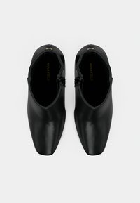 Pár černých kožených kotníkových bot se čtveratými špičkami a bočními zipy, zobrazených shora na bílém pozadí.