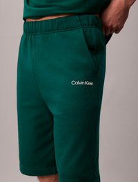 Shorts verts Calvin Klein fabriqués en mélange de coton doux, avec une taille élastique et des poches latérales, arborant un petit logo sur la cuisse gauche.