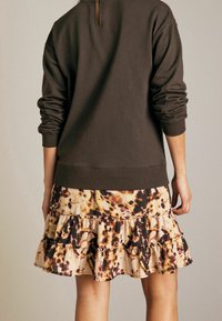 Sweatshirt marron foncé à manches longues, associé à une jupe à volants superposée ornée d'un motif abstrait audacieux en beige et marron foncé.