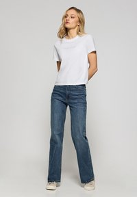 Vit bomull t-shirt med "Polo Club" tryck, kombinerat med blå jeans och beige sneakers. Jeansarna har rak benpassform och klassiska fickor.