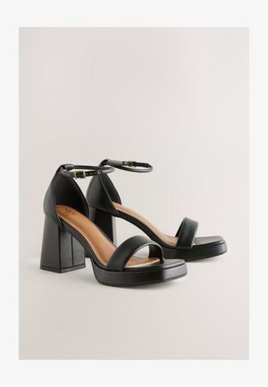 Sandalias de plataforma negras con tacón, correa en el tobillo, textura de cuero suave, tacones cuadrados gruesos y diseño de punta abierta.